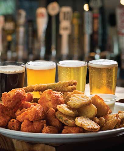 close up photo of craft beer behind a plat of fried food.