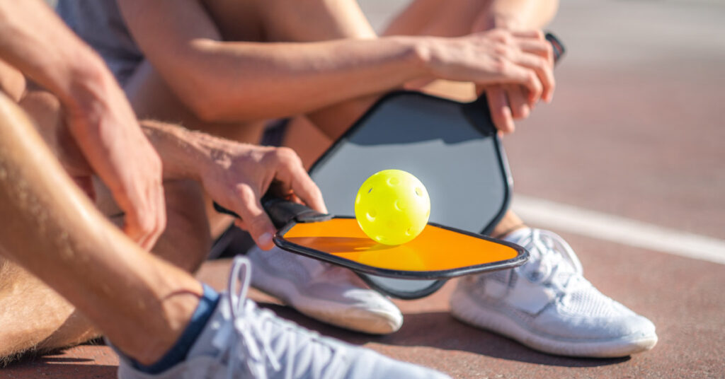 couple with yellow ball with paddle sitting after game, outdoor sport leisure activity.