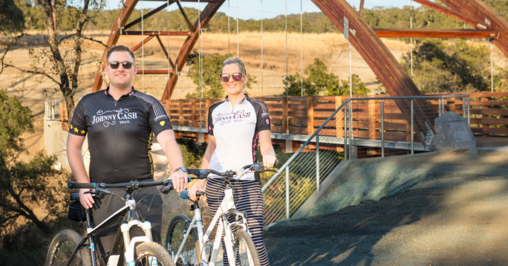 couple posing with their bikes in front of bridge in cycling apparel