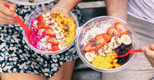 couple sitting together holding a couple of acai bowls