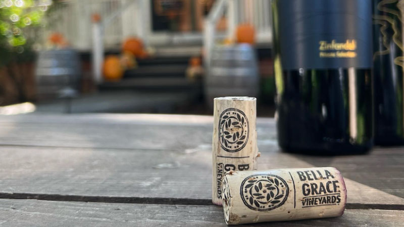a couple of wine corks on a wooden table with Bella Grace Vineyards in the background