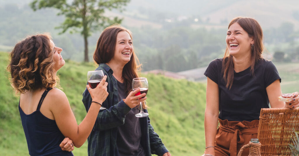 Three friends laughing while enjoying wine outdoors