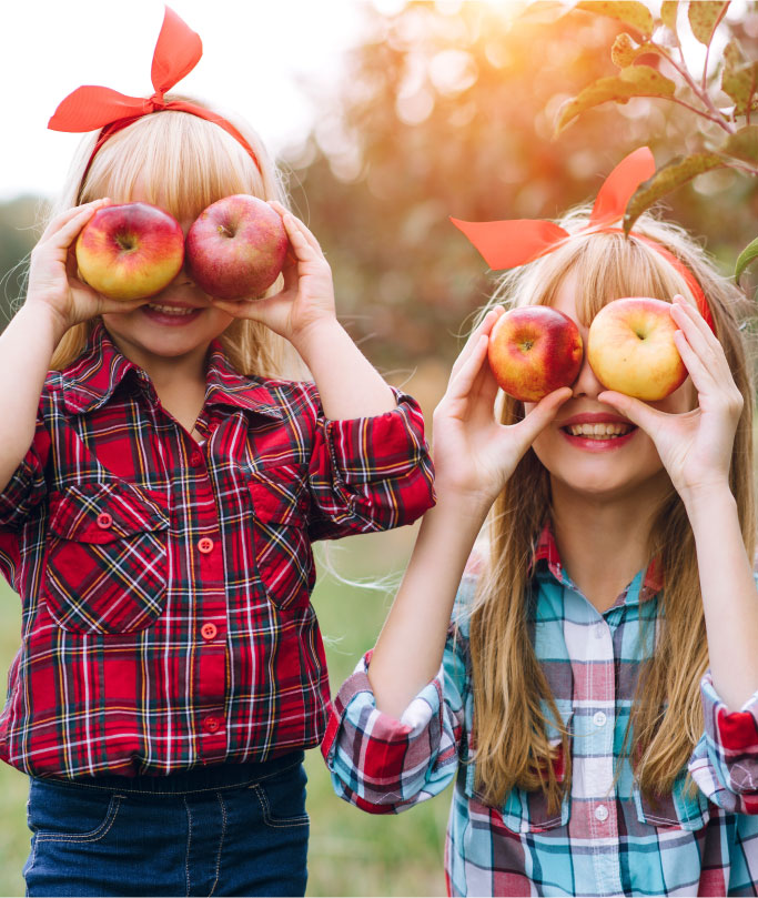 Sisters holding red apples to their eyes