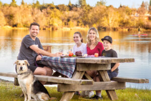 family of 4 and a dog having a picnic in front of a lake